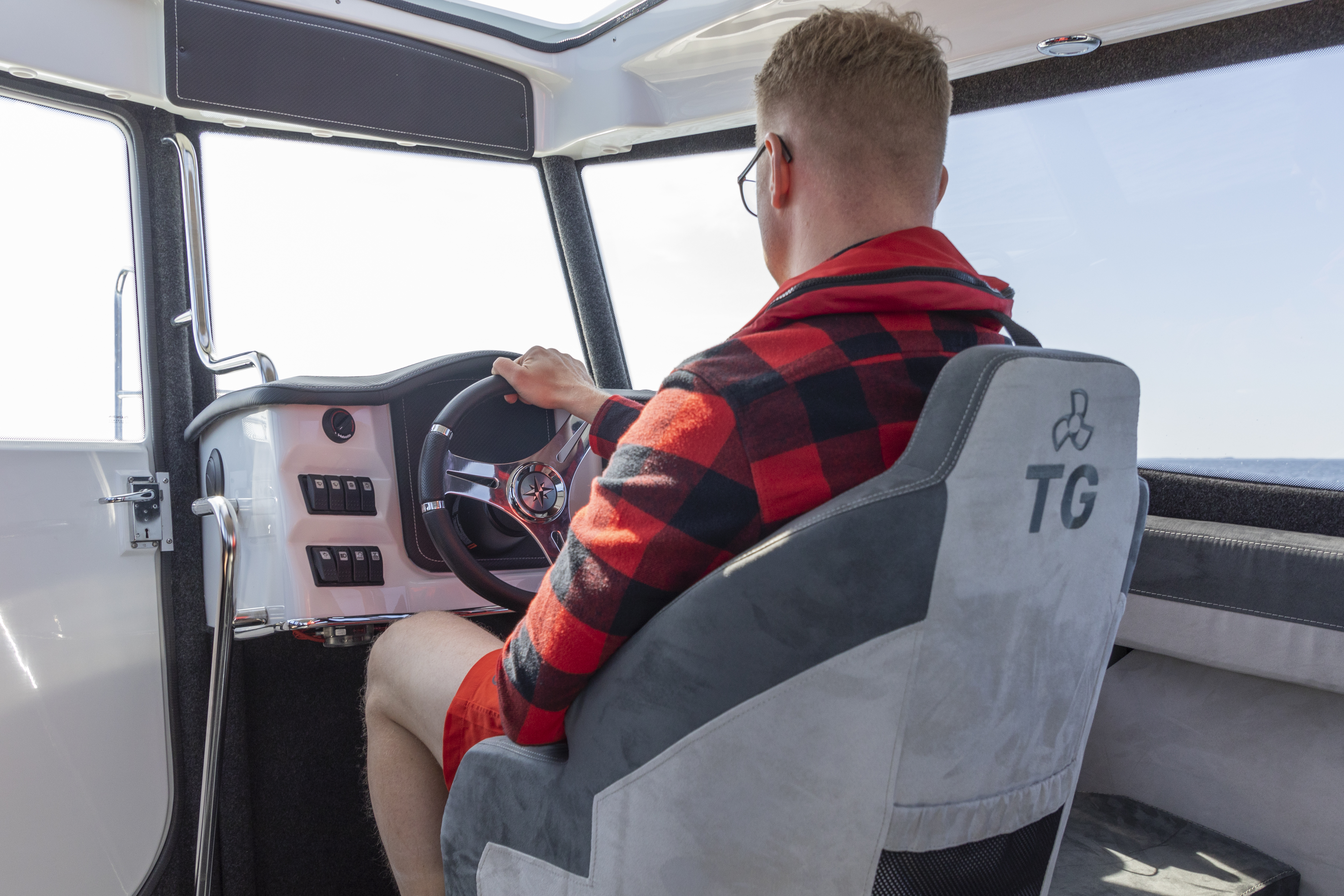 Man in checkered jacket enjoying the comfort of the TG cabin, driving the boat.