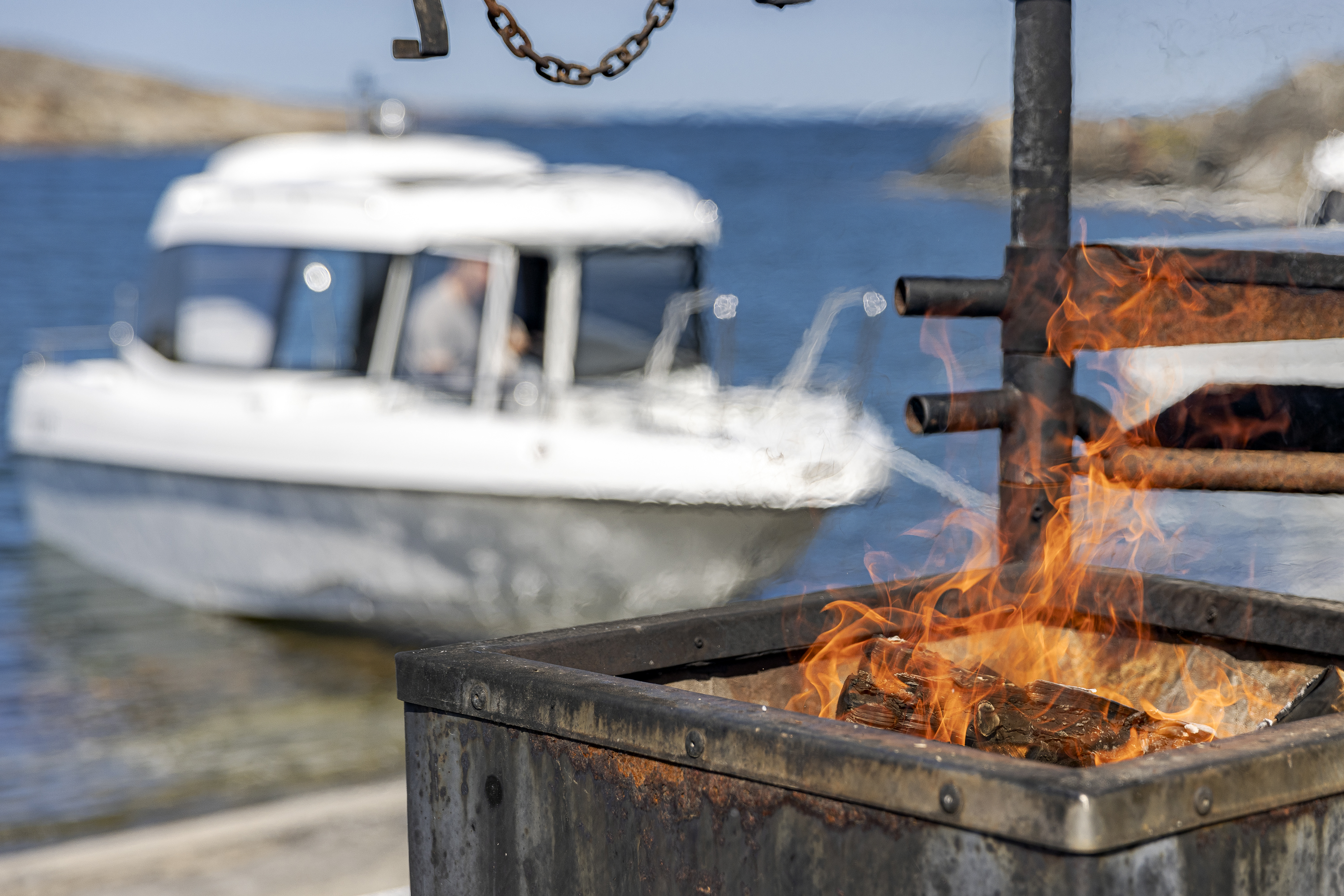 Open fire at a camping site in the Finnish archipelago. TG 6.9 cabin boat in the background.