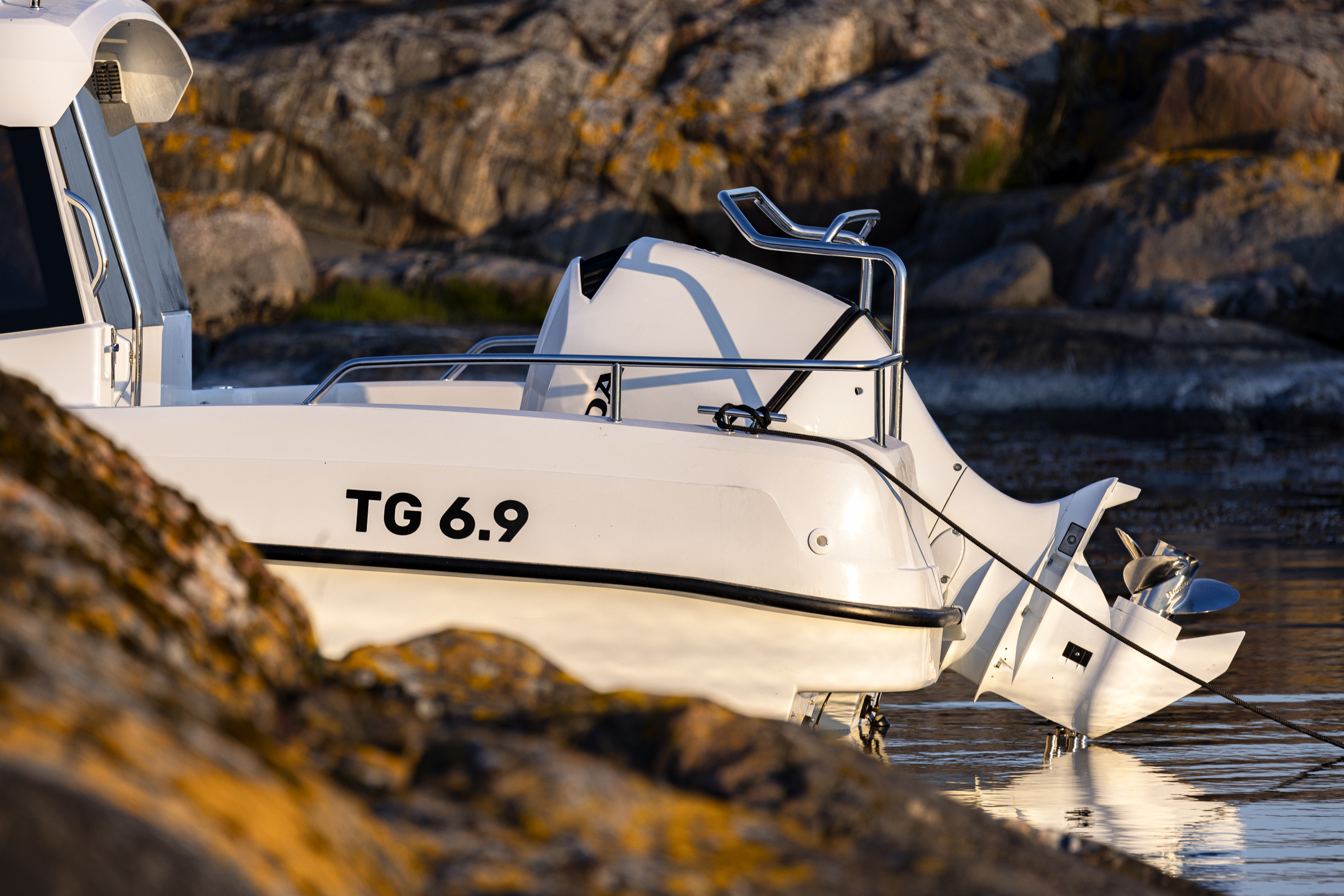 The stern part of the TG 6.9 cabin boat drenched in evening sun. White Honda outboard engine.